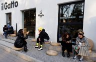 Várias pessoas sentadas em almofadas no chão, do lado de fora do café 'il Gatto'.