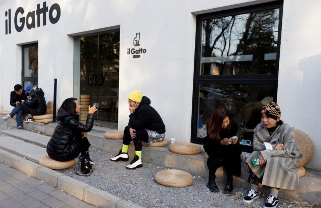 Várias pessoas sentadas em almofadas no chão, do lado de fora do café 'il Gatto'.