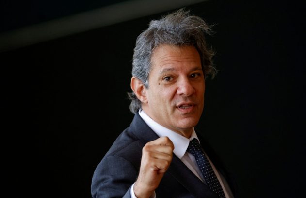 Homem de terno, cabelo grisalho, com punho cerrado e boca entreaberta, olha fixamente para a câmera.