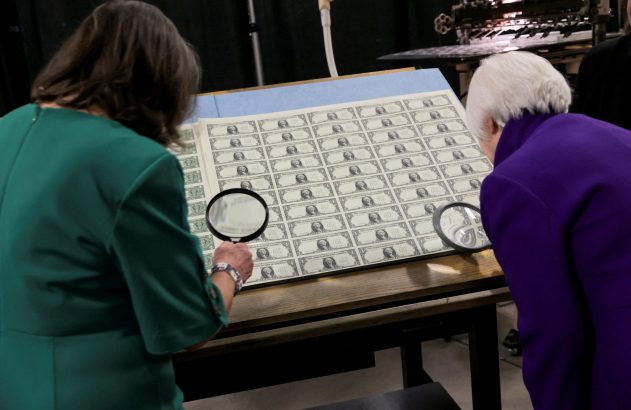 Duas pessoas observam uma folha de cédulas de um dólar com lupas.