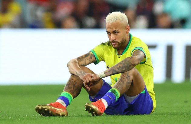 Neymar sentado no campo, de uniforme do Brasil, com expressão pensativa.