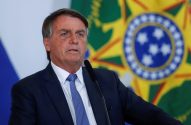 Jair Bolsonaro, de terno, discursa ao microfone com a bandeira do Brasil desfocada ao fundo.