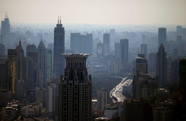 Panorâmica urbana com prédios altos, uma autoestrada cheia de carros e neblina ao longe.