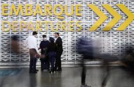 Pessoas em movimento em um saguão de aeroporto, com letreiro "EMBARQUE DEPARTURES" e setas amarelas.