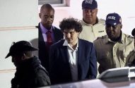 Sam Bankman-Fried é escoltado por policiais de uniforme e um homem de terno.