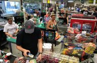 Cena de supermercado com clientes e funcionários nos caixas, processando compras em esteiras.