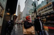 Pessoas em rua molhada de Nova York com sacolas de compras, Empire State Building e decorações de Natal.