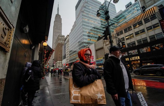 Pessoas em rua molhada de Nova York com sacolas de compras, Empire State Building e decorações de Natal.
