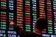 Pessoa aponta para cotações da bolsa em tela digital.