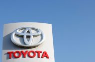 Sinal da Toyota em cinza e vermelho com logotipo prateado contra um céu azul claro.