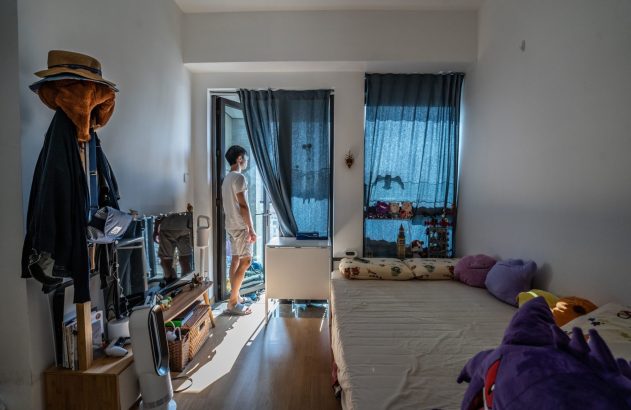 Jovem olha pela porta da varanda em um quarto iluminado pelo sol.