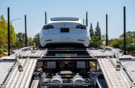Tesla branco sendo transportado em caminhão-cegonha. Vista traseira do carro no andar superior.