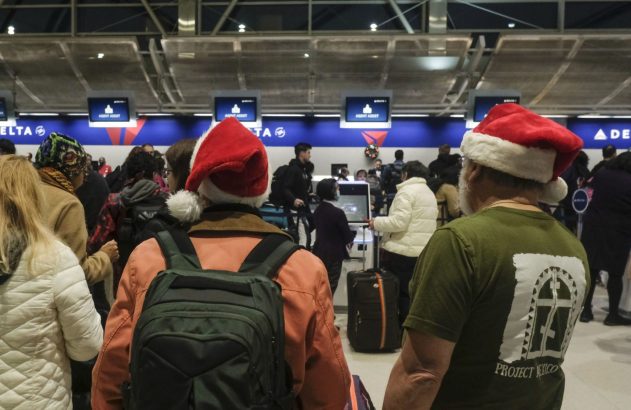 Pessoas com chapéus de Papai Noel e malas em uma área de check-in movimentada da Delta.