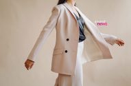 Pessoa de blazer rosa claro e calça, blusa escura, com braços abertos, em pose dinâmica.