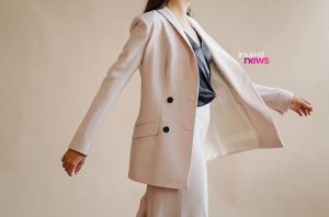 Pessoa de blazer rosa claro e calça, blusa escura, com braços abertos, em pose dinâmica.