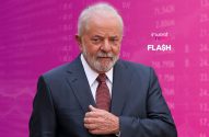 Lula, de terno e barba, olhando à frente, em um fundo com dados financeiros e o logo 'invest news FLASH'.