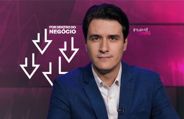 Homem em blazer azul em programa de notícias financeiras. Fundo roxo, setas para baixo, logos 'Por Dentro do Negócio', 'Invest News'.