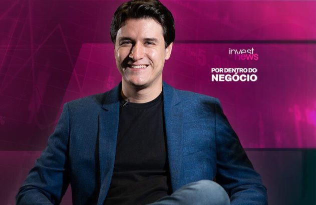 Homem sorridente de blazer azul, sentado. Ao fundo, roxo com gráficos e o logo "Invest News: Por Dentro do Negócio".