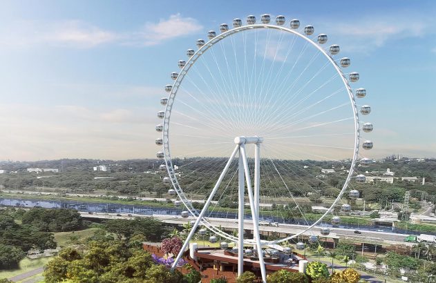 Grande roda-gigante branca em destaque. Ao fundo, paisagem urbana com rio, rodovia movimentada e áreas verdes.