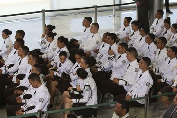 Cadetes uniformizados sentados em fileiras, prestando atenção.