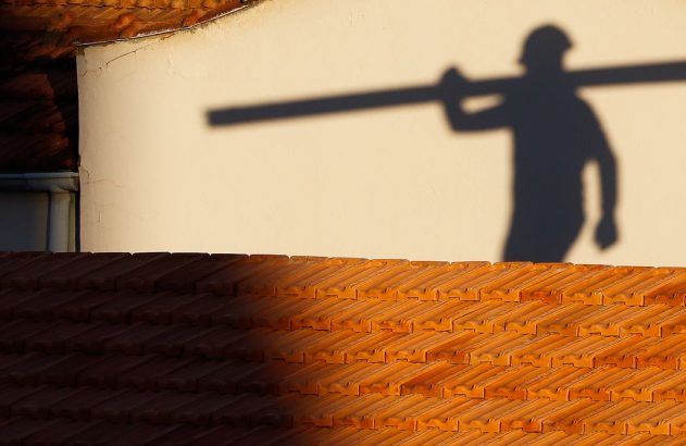 Sombra de trabalhador com viga no ombro em parede clara acima de telhado de telhas.