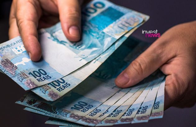 Mãos manuseiam e contam notas de 100 Reais, o dinheiro brasileiro.