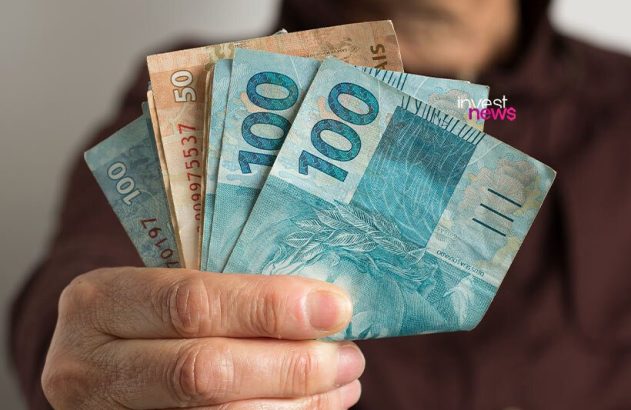 Mão segurando notas de Reais: R$100 e R$50.