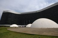 Edifício curvo do TSE com fachada escura de vidro. Múltiplas cúpulas brancas no gramado à frente.