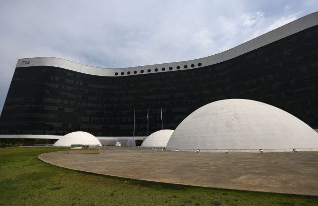 Edifício curvo do TSE com fachada escura de vidro. Múltiplas cúpulas brancas no gramado à frente.