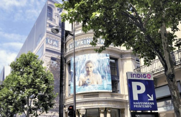 Fachada do Printemps Haussmann em Paris com grande anúncio e placa de estacionamento Indigo.
