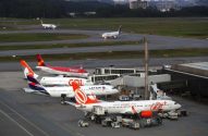 Pátio de aeroporto com aviões de passageiros sendo preparados para voo e outros taxiando.