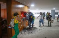 Pessoas em prédio público após vandalismo. Chão com detritos pretos, armário de incêndio quebrado.