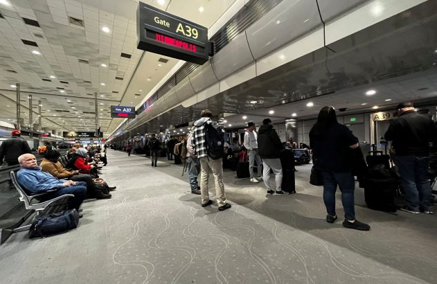 Pessoas aguardam embarque no Gate A39 para Minneapolis em um aeroporto, com outros passageiros sentados ao lado.