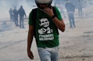 Homem de capacete e camisa verde "Presidente Bolsonaro" caminha em ambiente enfumaçado com silhuetas ao fundo.