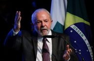 Presidente Lula discursa com microfone, gesticulando, diante da bandeira do Brasil.