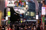 Multidão em rua de Shibuya, Japão, sob arco luminoso com placas "Center-Gai". Pessoas usam máscaras. Cena urbana movimentada.