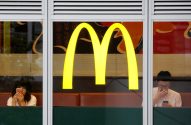 Logo amarelo do McDonald's em janela; dois clientes usam celulares lá dentro.