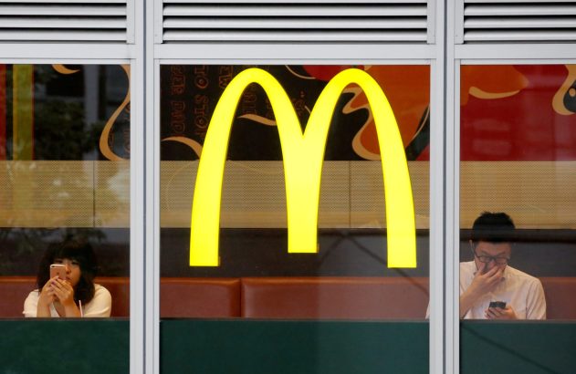 Logo amarelo do McDonald's em janela; dois clientes usam celulares lá dentro.