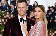 Tom Brady e Gisele Bündchen sorrindo. Gisele, de vestido rosa, toca o terno bordô de Tom.