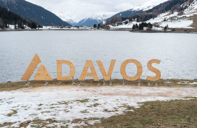 Vista de inverno do lago Davos e das letras de madeira "DAVOS" em primeiro plano, com montanhas nevadas.
