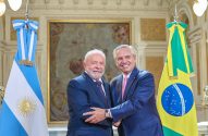 Lula e Alberto Fernández sorriem em encontro, com bandeiras do Brasil e Argentina ao fundo.