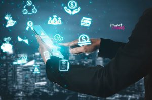 Mãos interagem com smartphone. Ícones financeiros digitais luminosos (moedas, gráficos, dinheiro) cercam a tela. Fundo urbano.