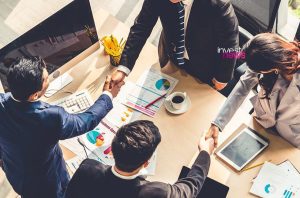 Vista aérea de reunião de negócios. Duas duplas apertando as mãos sobre mesa com gráficos.