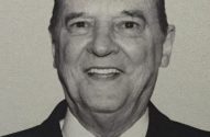 Homem idoso, em terno e gravata, sorrindo em foto P&B.