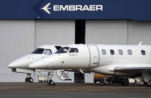 dois aviões posicionados um ao lado do outro com a logo da Embraer acima