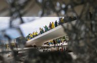 Cena através de vidro quebrado: manifestantes com bandeiras do Brasil em rampa, com sinais de vandalismo abaixo.