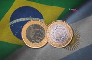 Moeda de 1 Real brasileiro e moeda argentina sobrepostas, sobre as bandeiras do Brasil e da Argentina.