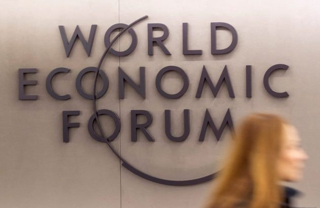 Pessoa desfocada em movimento diante do letreiro "WORLD ECONOMIC FORUM" na parede.