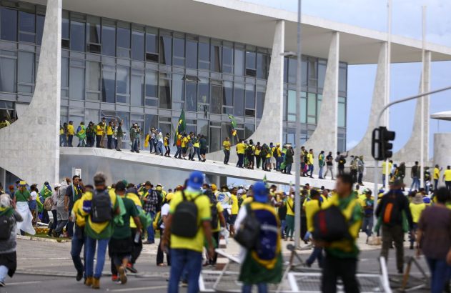 Manifestantes vestidos de verde e amarelo com bandeiras do Brasil em edifício governamental.