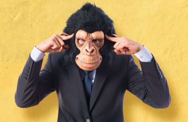 Homem de terno com máscara de gorila, dedos nas têmporas, em gesto de concentração.